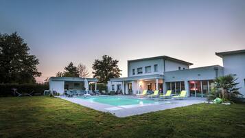 Relax by the pool in a serene outdoor space surrounded by a lawn and trees.