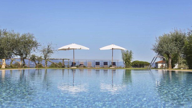 A clear swimming pool with lounge chairs and umbrellas, surrounded by trees and a clear sky. - Wonderful private villa with A/C, WIFI, private pool, TV, veranda and panoramic view, close to L... (Colle Di Compito)