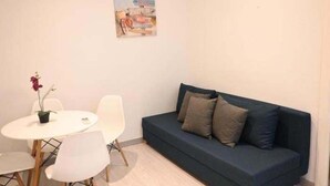A room with a blue sofa, white chairs, a small table with a potted plant, and a wall-mounted picture. - Homenfun Barcelona Les Corts (Barcelona)