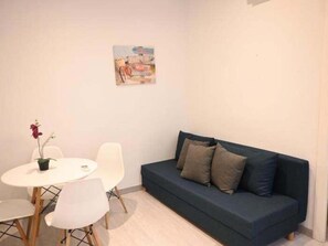 Ein kleines Zimmer mit einem dunkelblauen Sofa, einem weißen runden Tisch mit zwei Stühlen und einem einzelnen Blumentopf.