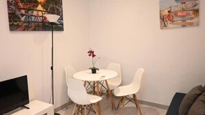 A room with a round table, four white chairs, a potted plant, a flat-screen TV on a white stand, and two paintings on the walls. - Homenfun Barcelona Les Corts (Barcelona)