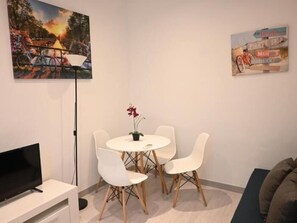 Ein Zimmer mit einem runden Esstisch, vier Stühlen, einem Flachbildfernseher, einer Stehlampe und zwei Wandbildern.