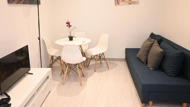 A room with a TV, a white table with chairs, a blue sofa, and two wall-mounted artworks. - Homenfun Barcelona Les Corts (Barcelona)