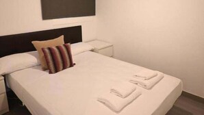 A neatly made bed with white linens and two folded towels, a dark headboard, a bedside table, and a wall-mounted light fixture. - Homenfun Barcelona Les Corts (Barcelona)