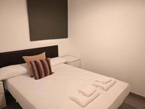 Ein Hotelzimmer mit Bett, Kissen, Nachttisch und einem an der Wand befestigten Kunstwerk.