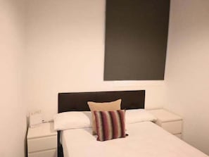 Une chambre d’hôtel comprenant un lit, une table de chevet, une lampe et un panneau fixé au mur.