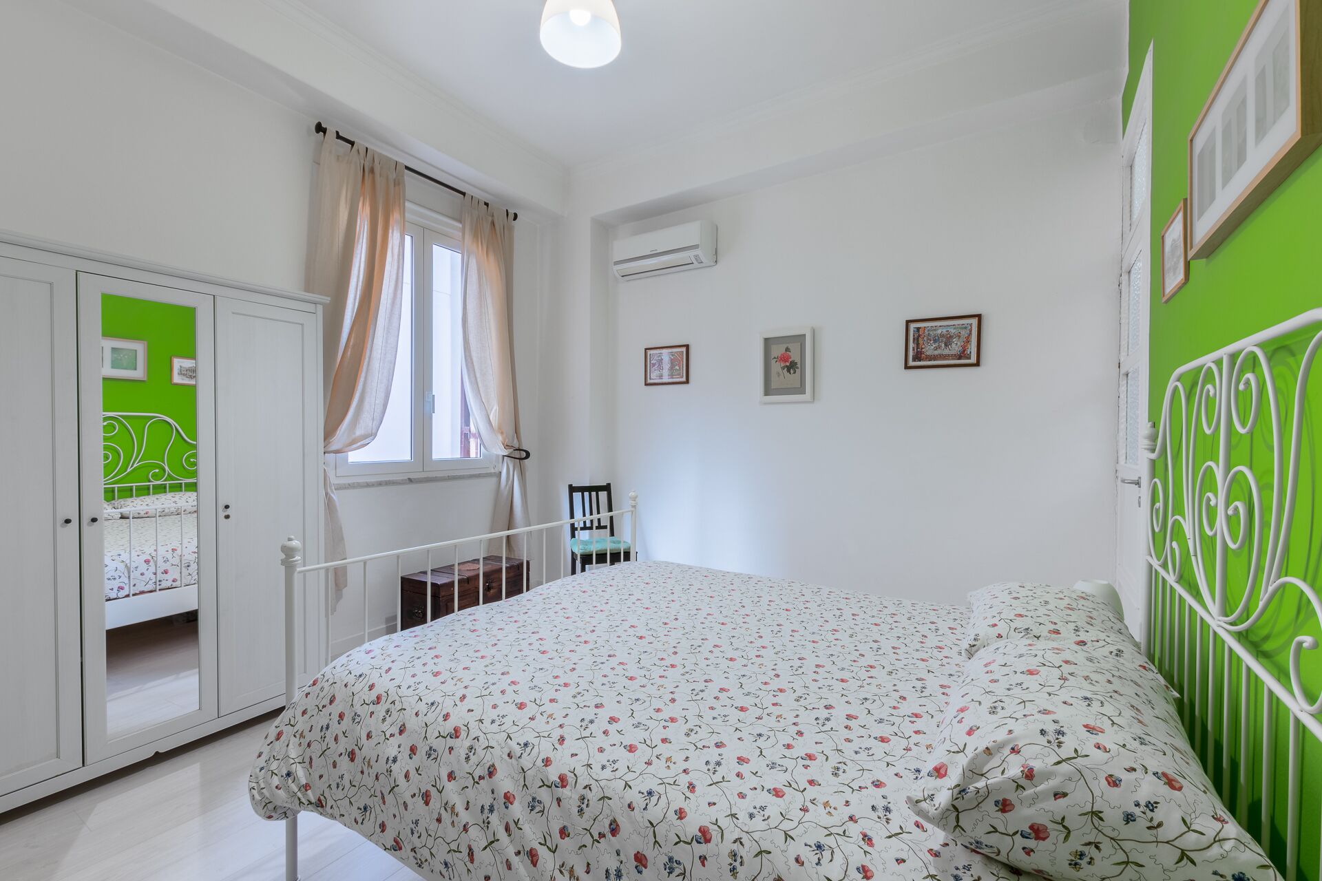 A bedroom with a bed, a wardrobe, a window with curtains, a chair, and a green wall.
