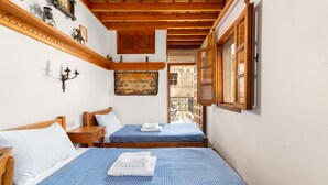 A hotel room with two beds, wooden headboards, a wooden ceiling, a wall-mounted lamp, and a window with a view of the outside. - Traditional 17th Century Lindos Captains House

 (Lindos)