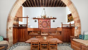 A traditional room with a wooden dining table, chairs, and a large tapestry hanging on the wall. - Traditional 17th Century Lindos Captains House

 (Lindos)