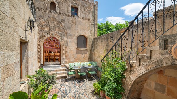 A courtyard with a stone building, a staircase, and outdoor seating. - Traditional 17th Century Lindos Captains House

 (Lindos)
