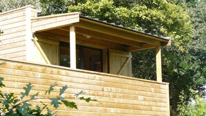 A wooden cabin with a balcony, surrounded by greenery.