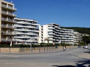 A multi-story hotel with balconies, a restaurant, and a street with vehicles and a pedestrian. - ROCAMAURA III BX-9 (Estartit)