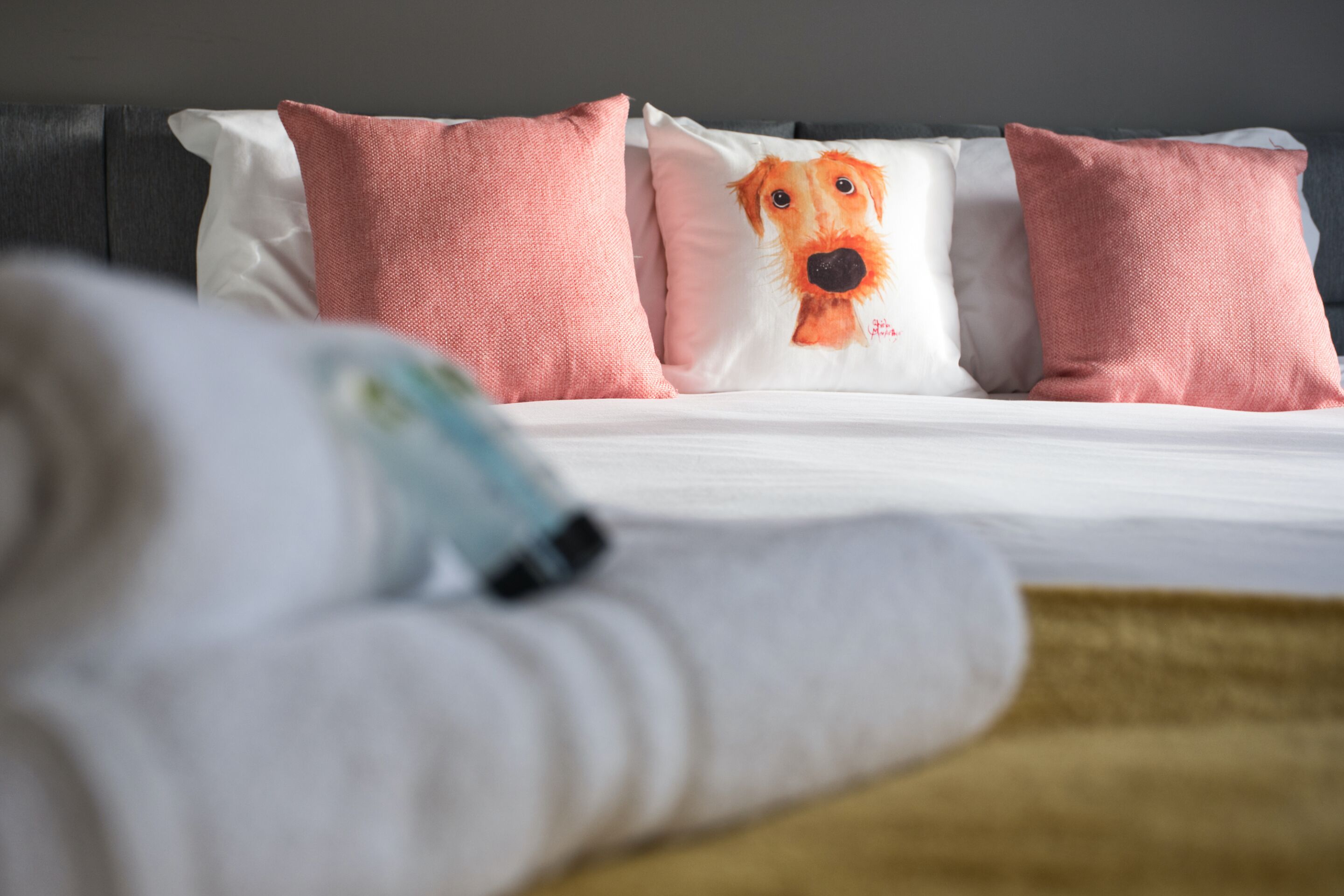 Un lit avec des oreillers roses et un coussin orné d’une illustration de chien.