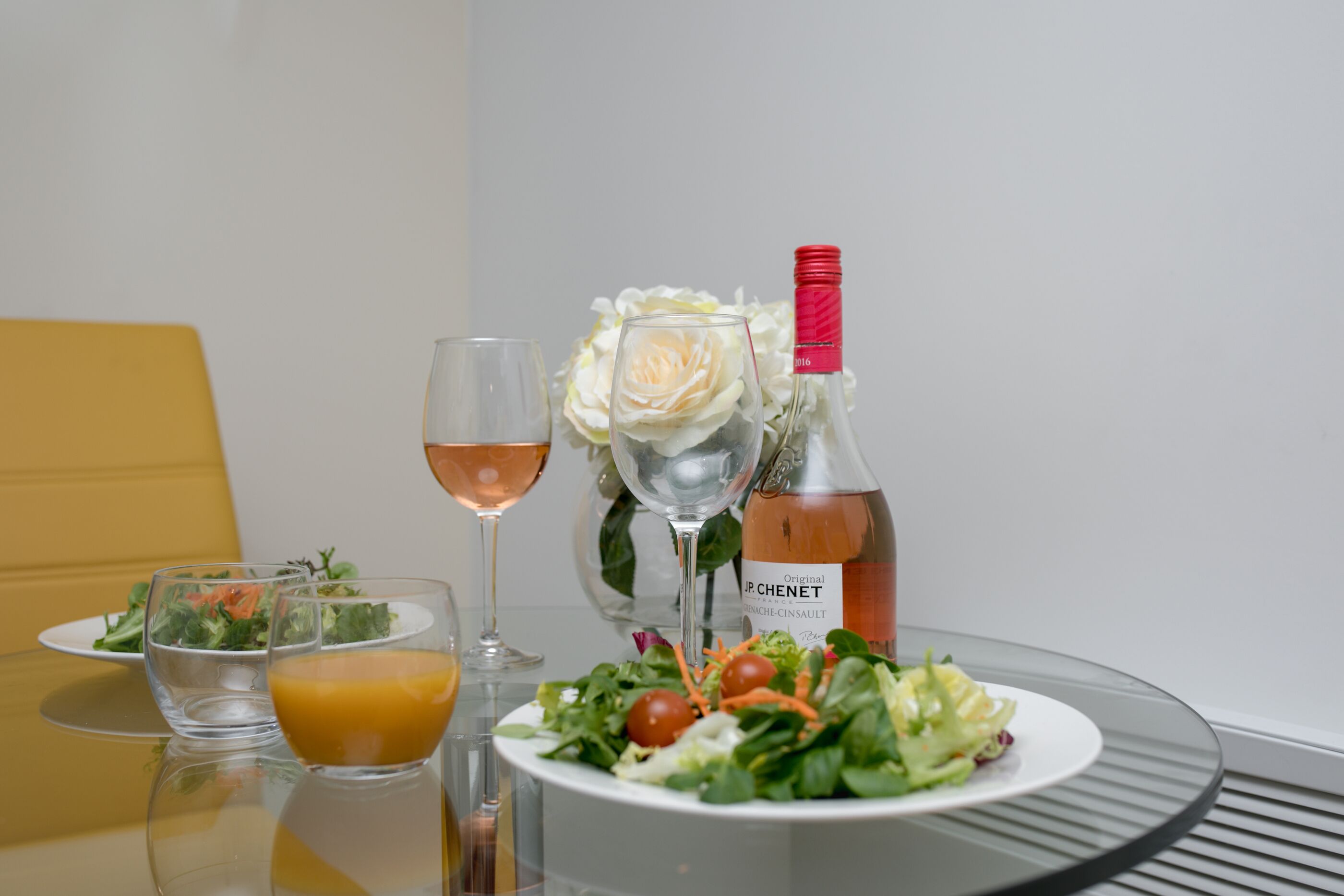 A table with a salad, two glasses of juice, a bottle of wine, and a glass of rosé wine.