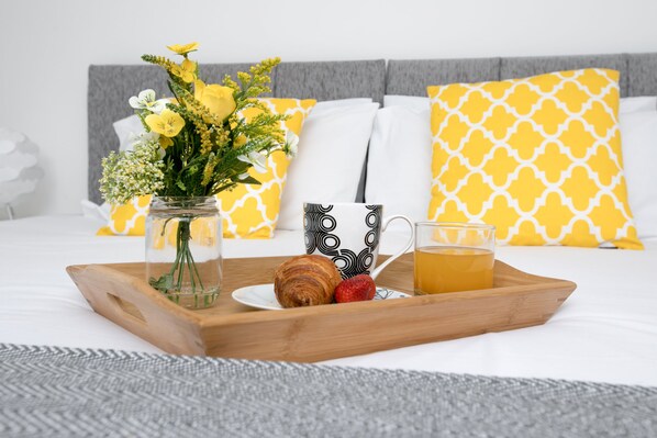 A breakfast tray with a croissant, a glass of orange juice, and a vase of flowers on a bed with patterned pillows.