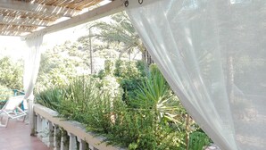 A covered outdoor area with a concrete bench, lush greenery, and a pergola structure.