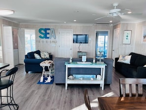 A modern living room with a TV, a sofa, a coffee table, and a dining area with chairs.