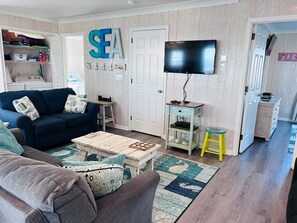 Een woonkamer met een bank, salontafel, televisie en een muur met een 'SEA' bord.