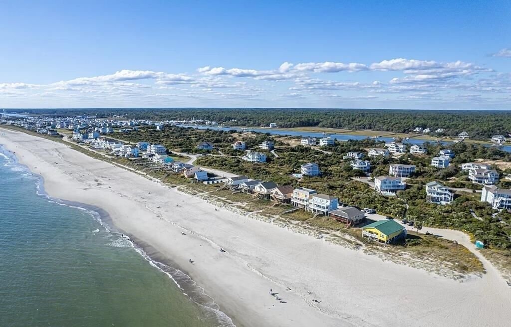 Ett bostadsområde vid kusten med hus som ligger längs stranden, en klar himmel och en vattenyta.