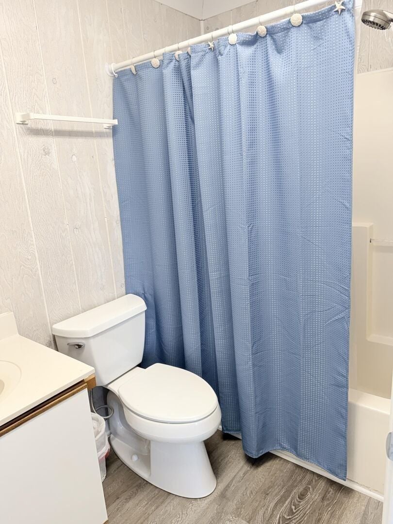 A bathroom with a white toilet, a shower curtain, and a wooden floor.