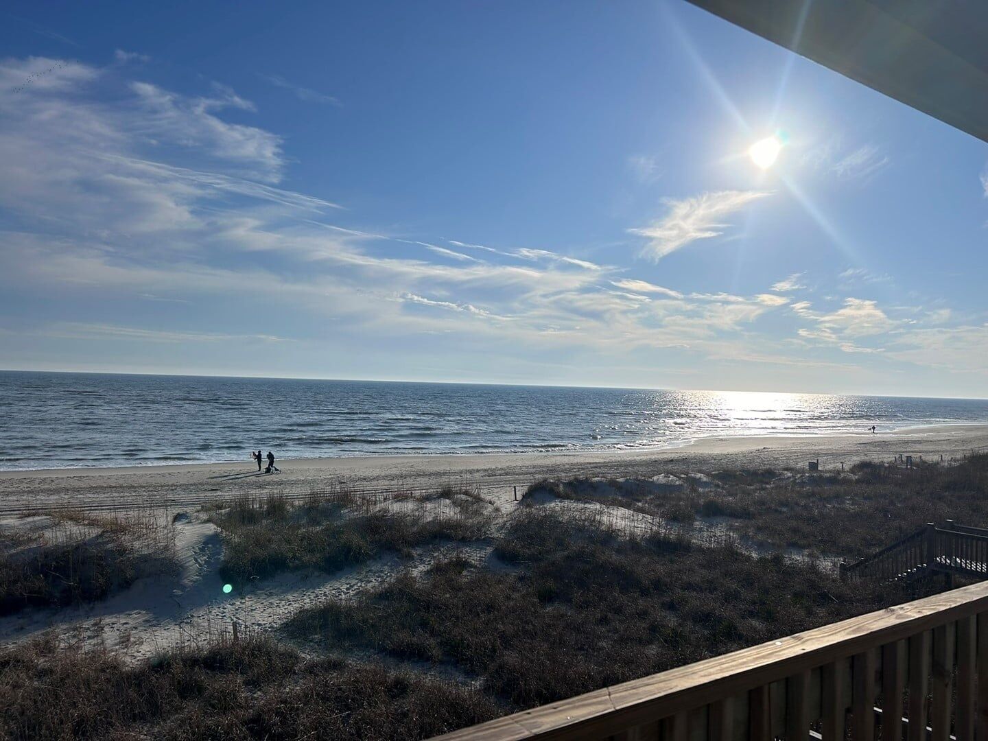 A beach view with a wooden deck, ocean, and clear sky.
