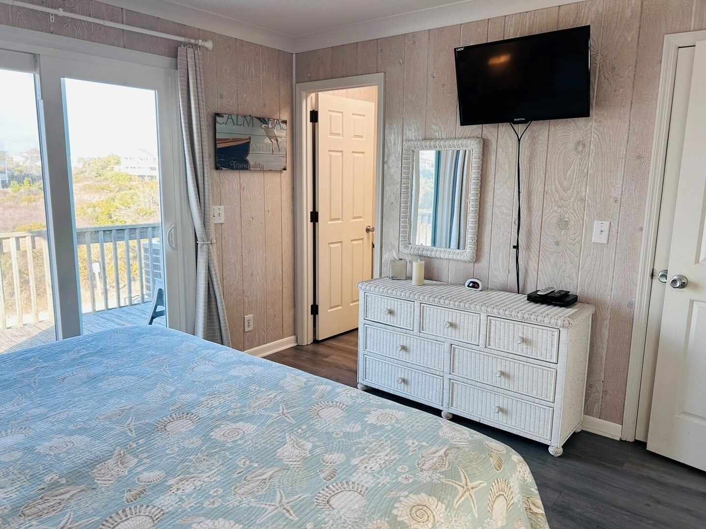 A bedroom with a bed, a dresser, a television, and a door leading to another room.