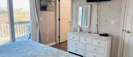 A bedroom with a bed, a dresser, a television, and a door leading to another room.