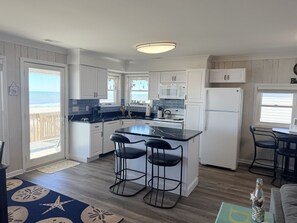 A modern kitchen with a central island, bar stools, and a view of the beach.