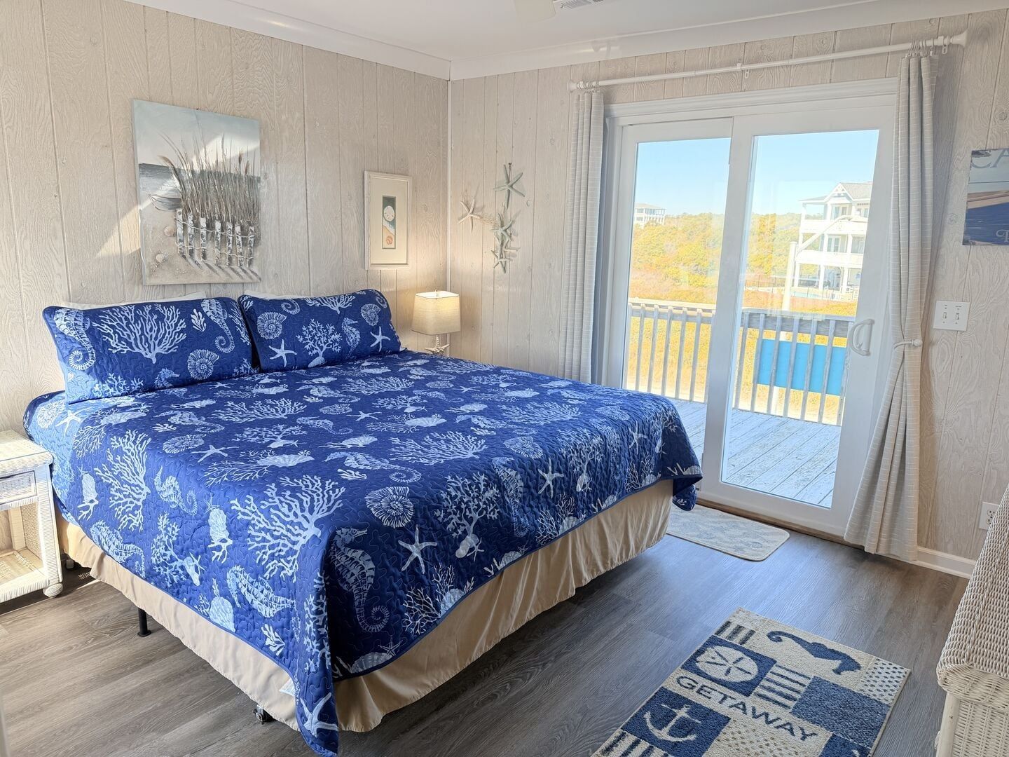 A bedroom with a large bed, a nightstand, a lamp, and a view of the outside through a sliding door.
