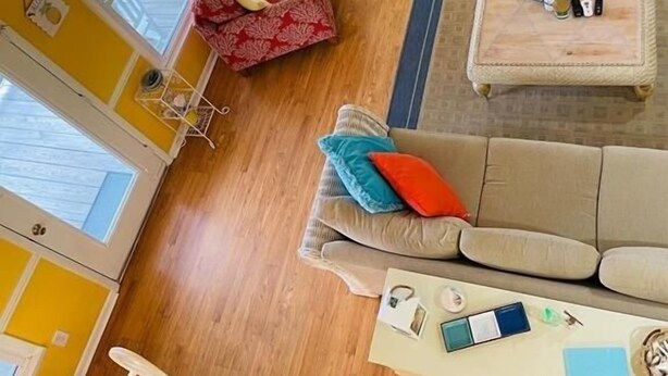 A bright yellow room with a ceiling fan, a sofa, a coffee table, and a dining table with chairs. - Beach Bells 4 Bedroom Home by RedAwning (Supply)