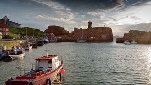 A harbor with boats, a lighthouse, and a large rock formation. - Unique 2 Bedroom Harbour Front Apartment. License No. EL00051F.     (Dunbar)