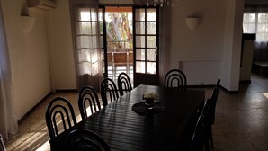A dining area with a wooden table and chairs, a vase with flowers, and a view through a window to the outside. - Stone bastide in a peaceful, closed park 700 m from the beach  (Porto-Vecchio)