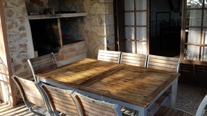 A rustic outdoor dining area with a stone wall, wooden table, and metal chairs. - Stone bastide in a peaceful, closed park 700 m from the beach  (Porto-Vecchio)