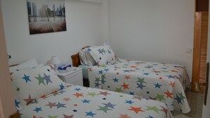 Una habitación con dos camas, cada una con ropa de cama estampada con motivos de estrellas, una mesita de noche con lámpara y un cuadro con una vista de la ciudad en la pared.