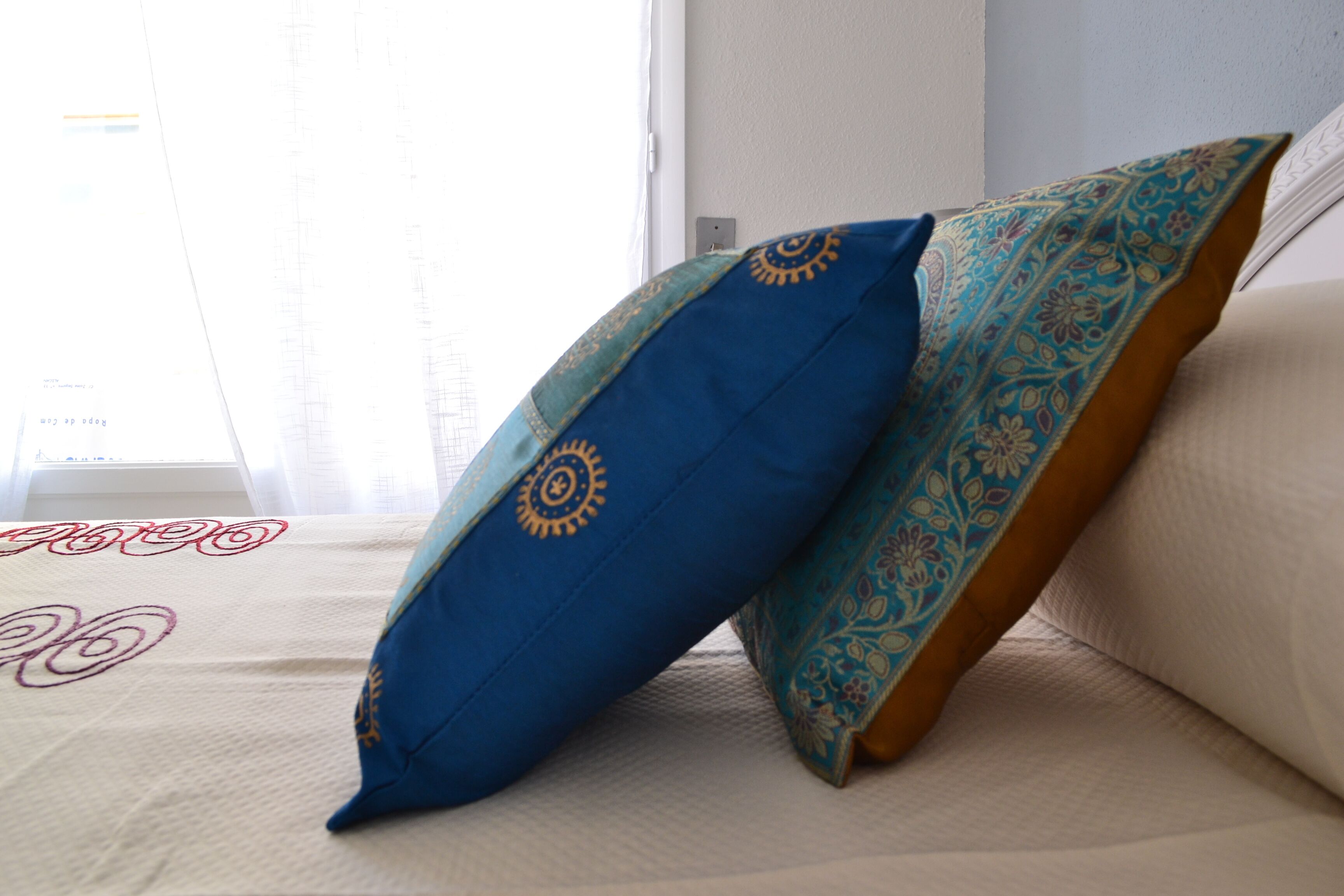 A bed with two pillows, one blue and one with a paisley pattern.