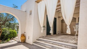 Un patio con escalones que conducen a una zona cubierta, un jarrón grande y una pequeña mesa con una planta.