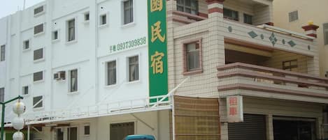 A building with a green vertical sign, multiple windows, and a garage area with parked vehicles.