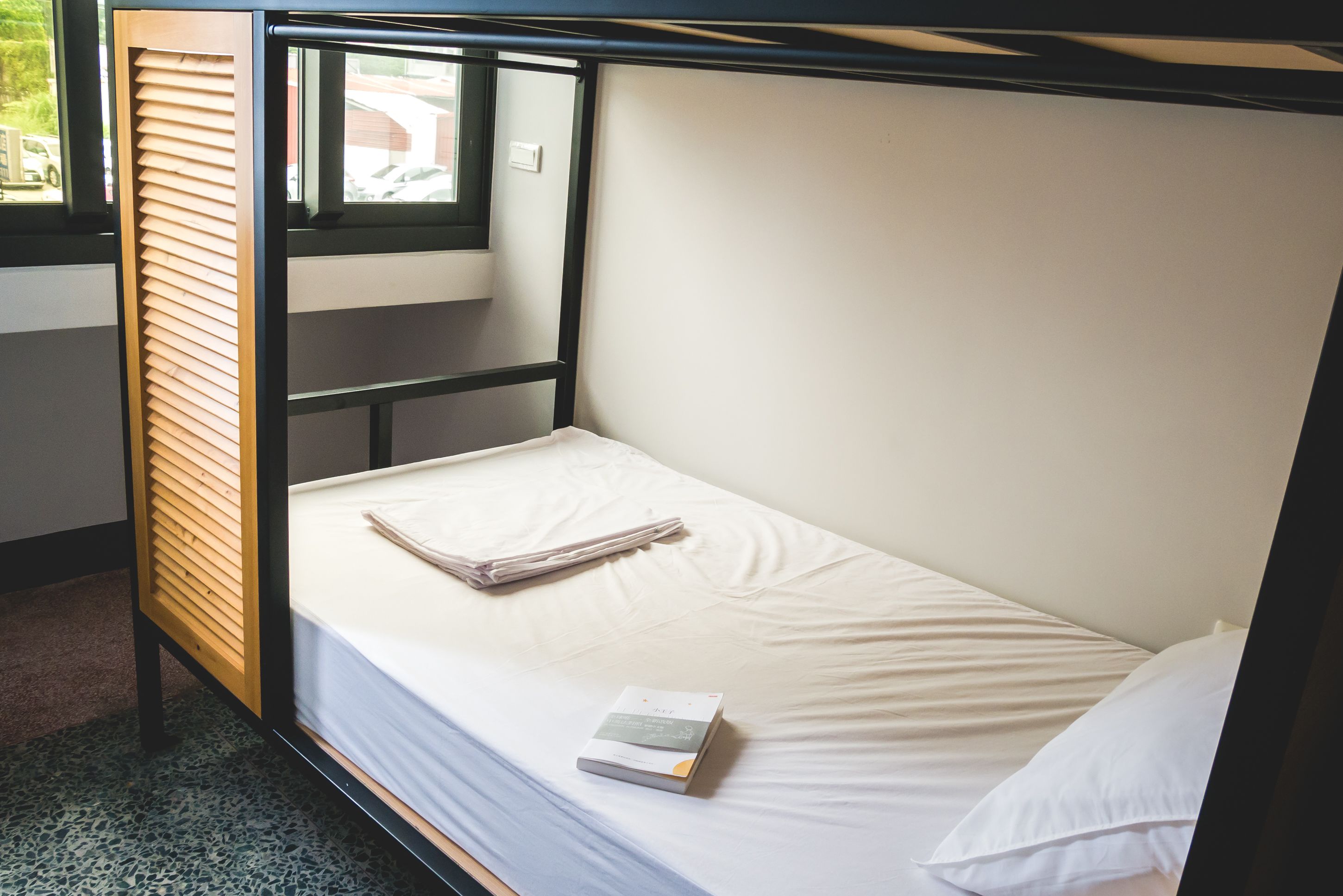 A single bed with a wooden headboard, a window, and a bedside table with a book.