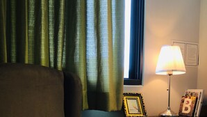 A room with a dark armchair, a lamp, and a small table with a picture frame and a lamp. - World Inn - Hostel (Hualien City)