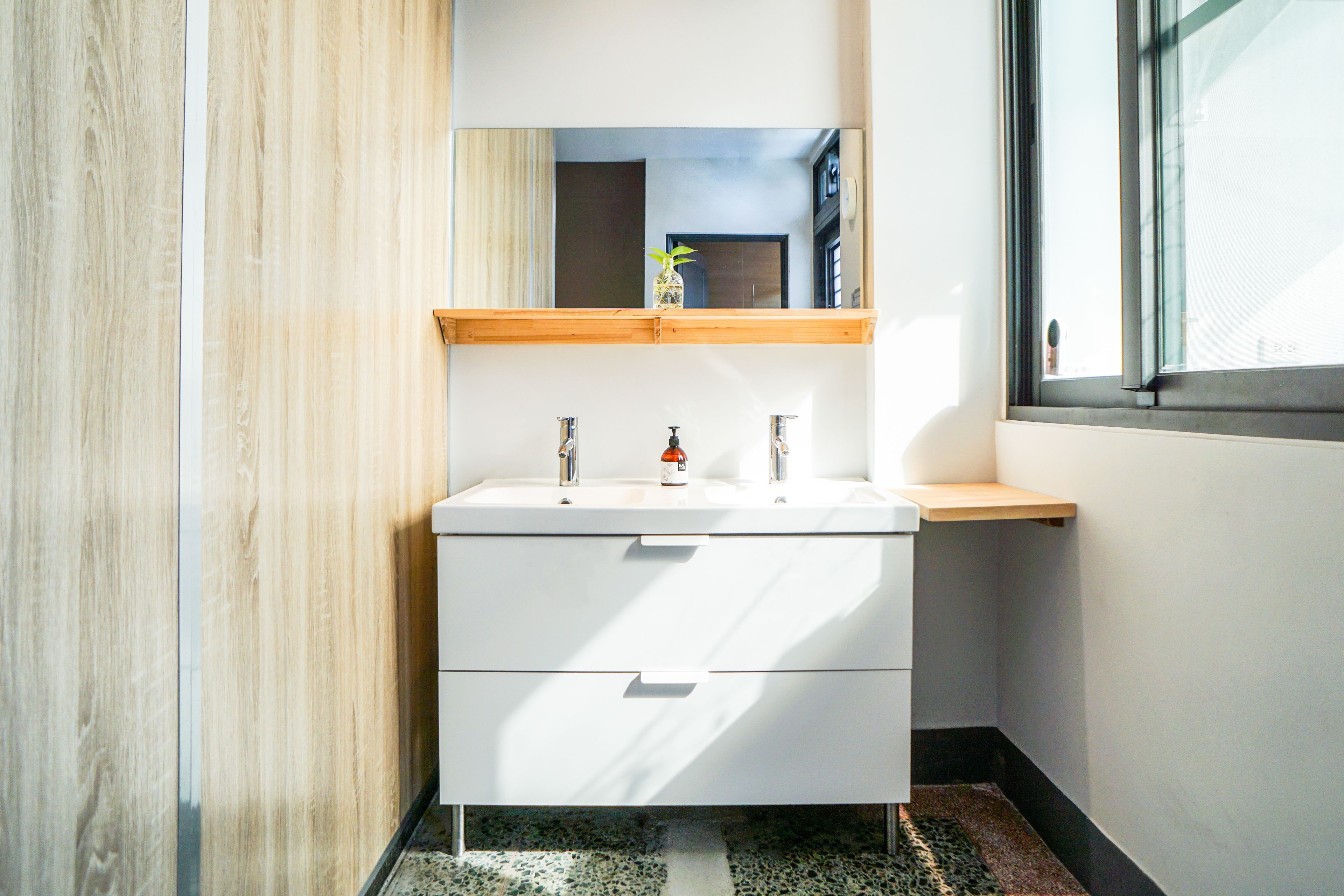 A modern bathroom with a white vanity, two sinks, a mirror, and a wooden shelf above the sink.