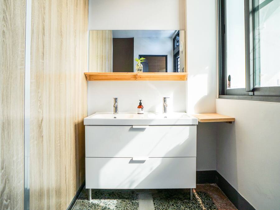 A modern bathroom with a white vanity, two sinks, a mirror, and a wooden shelf above the sink.