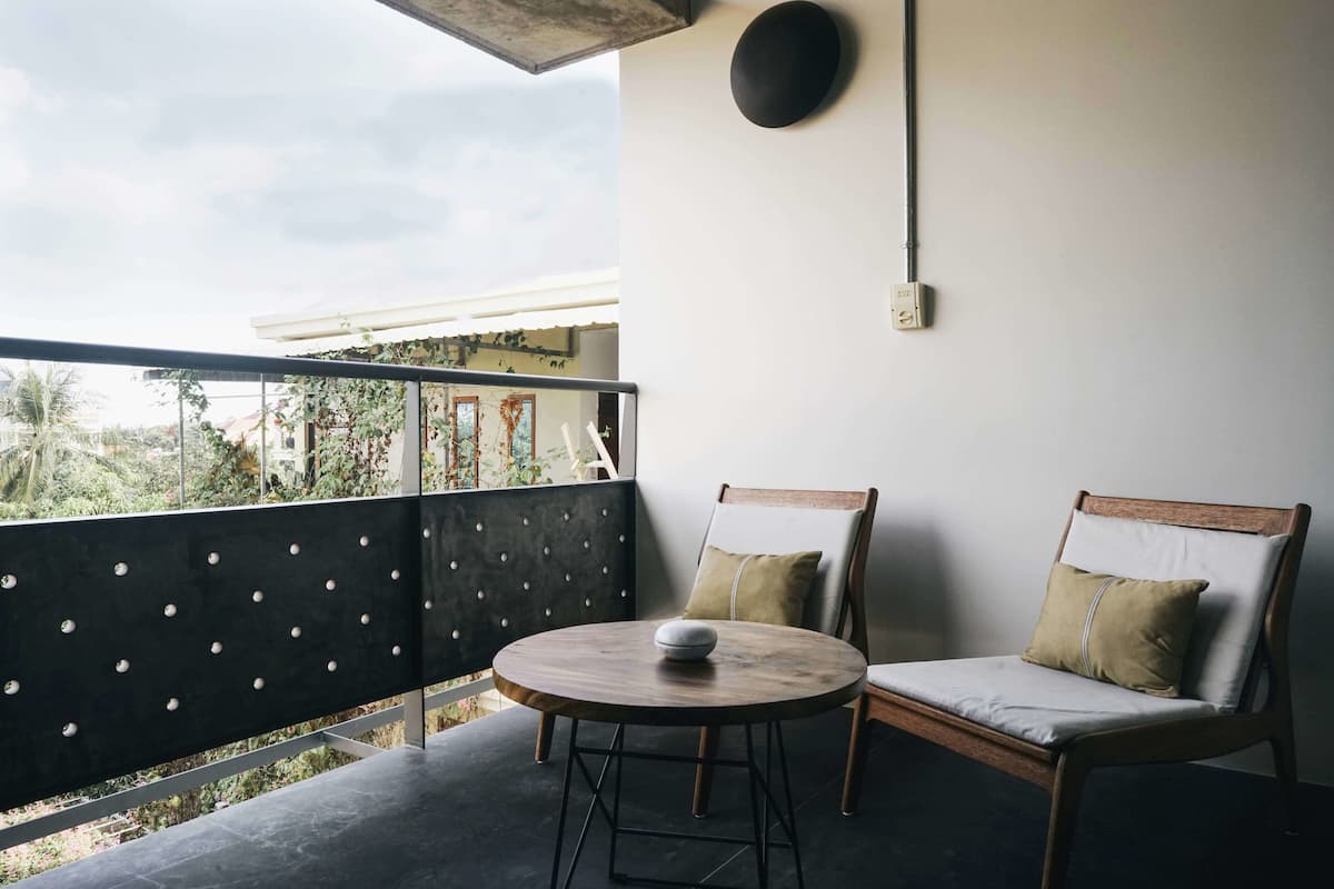 Un balcon avec une table ronde et deux chaises, une vue sur la verdure et un luminaire fixé au mur.