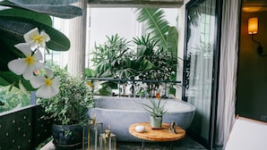A balcony with a round wooden table, a potted plant, a bathtub, and a view of lush greenery. - Urban Residences - Siem Reap (Siem Reap)