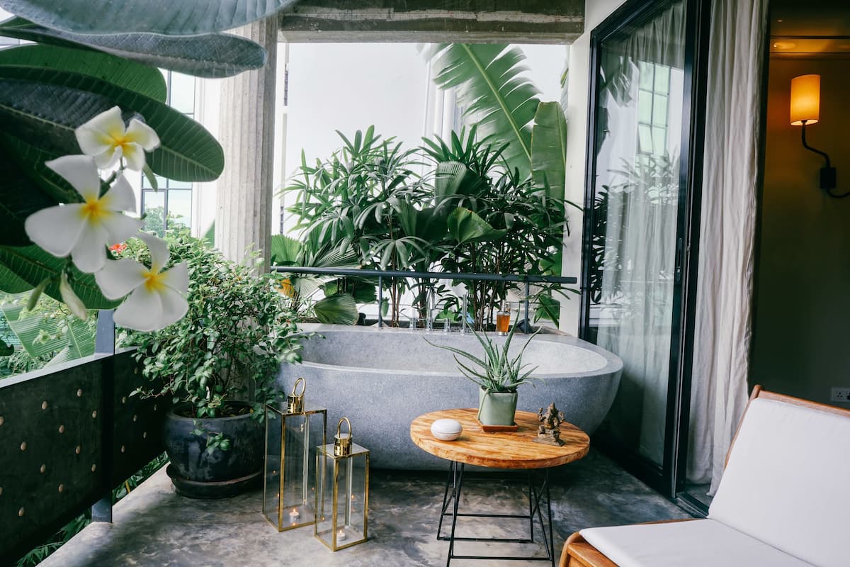 Un balcon avec une table ronde en bois, une plante en pot, une baignoire et une vue sur une végétation luxuriante.