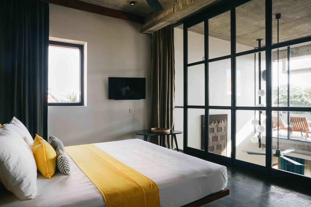 Une chambre d’hôtel moderne dotée d’un grand lit, d’une télévision à écran plat, d’une vue sur l’extérieur et d’un balcon avec des sièges.