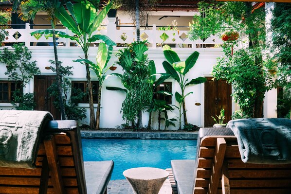 A poolside area with wooden lounge chairs, a stone table, and lush greenery.