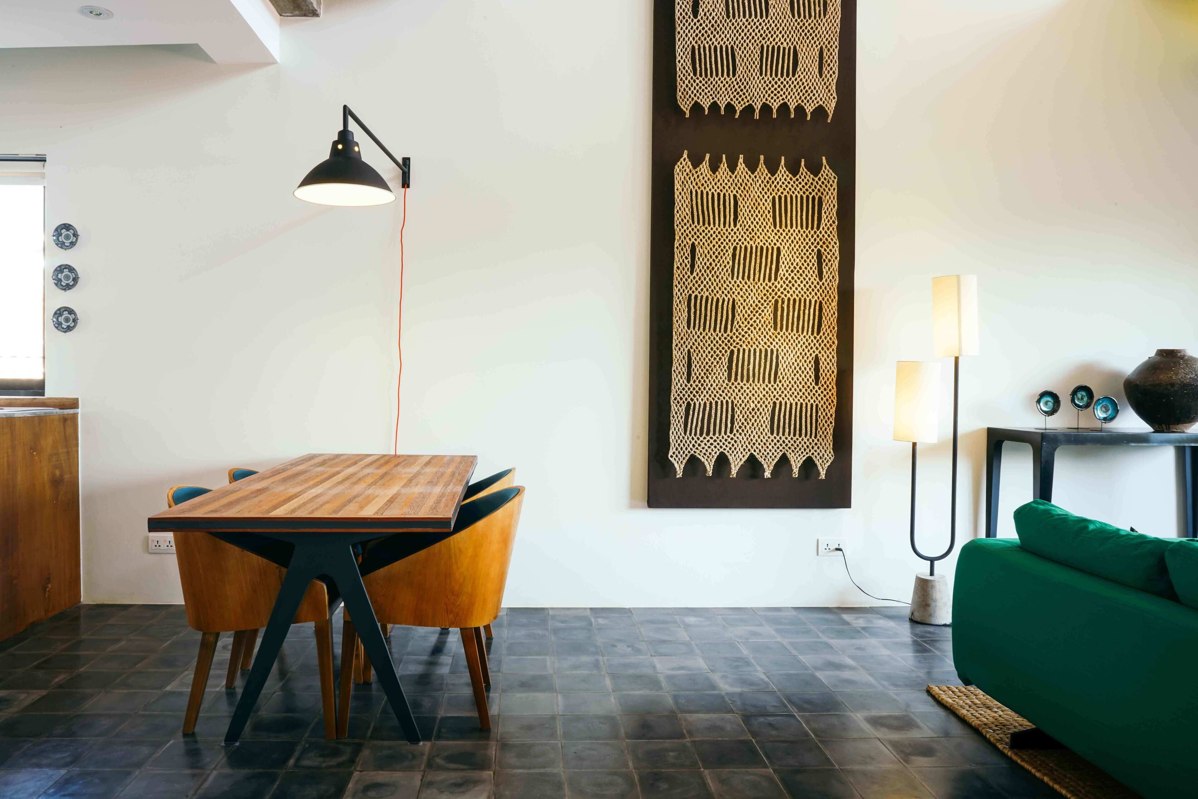 A modern dining area with a wooden table and chairs, a black pendant lamp, and a decorative wall piece.