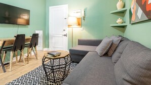 Un salon avec un canapé, une table basse et un téléviseur. On y trouve une porte, une lampe et un tableau au mur.