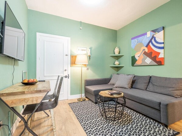 Ein Wohnzimmer mit grauem Sofa, einem Couchtisch, einem gemusterten Teppich und einem Bild an der Wand.