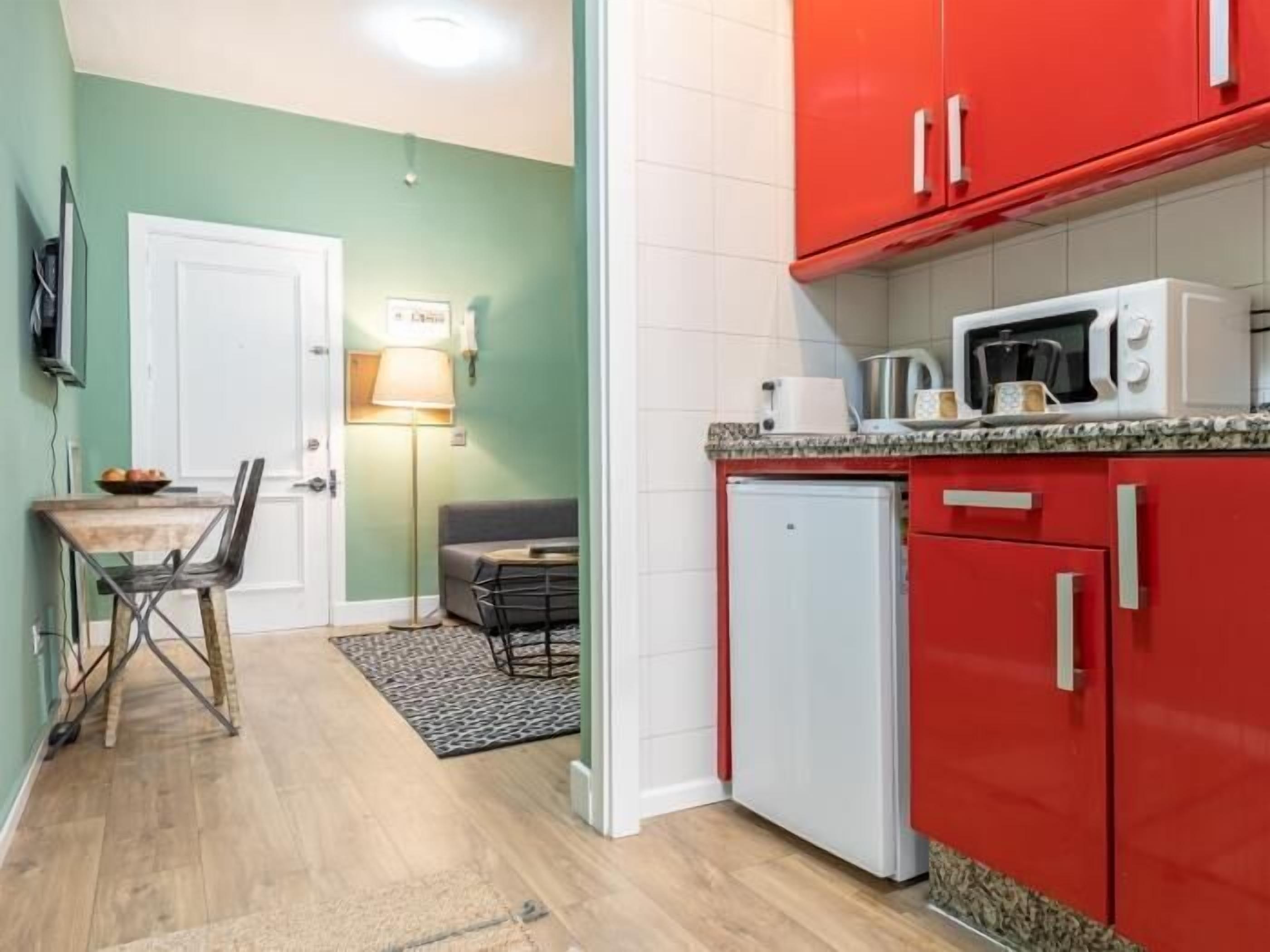 A compact kitchen with red cabinets, a white refrigerator, and a microwave on the countertop.